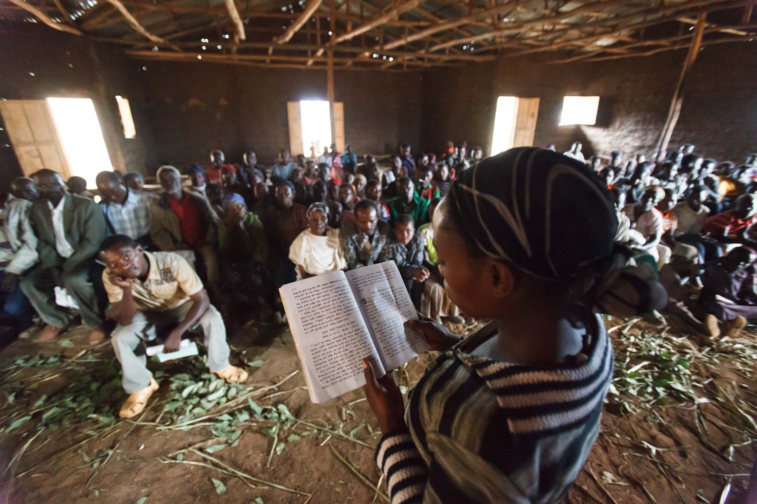 Ethiopian church congregation listens intently to woman reading Scriptures in their language.